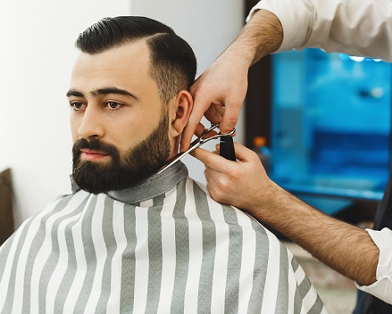 Image of a male client sitting in a barber chair having beard trimmed